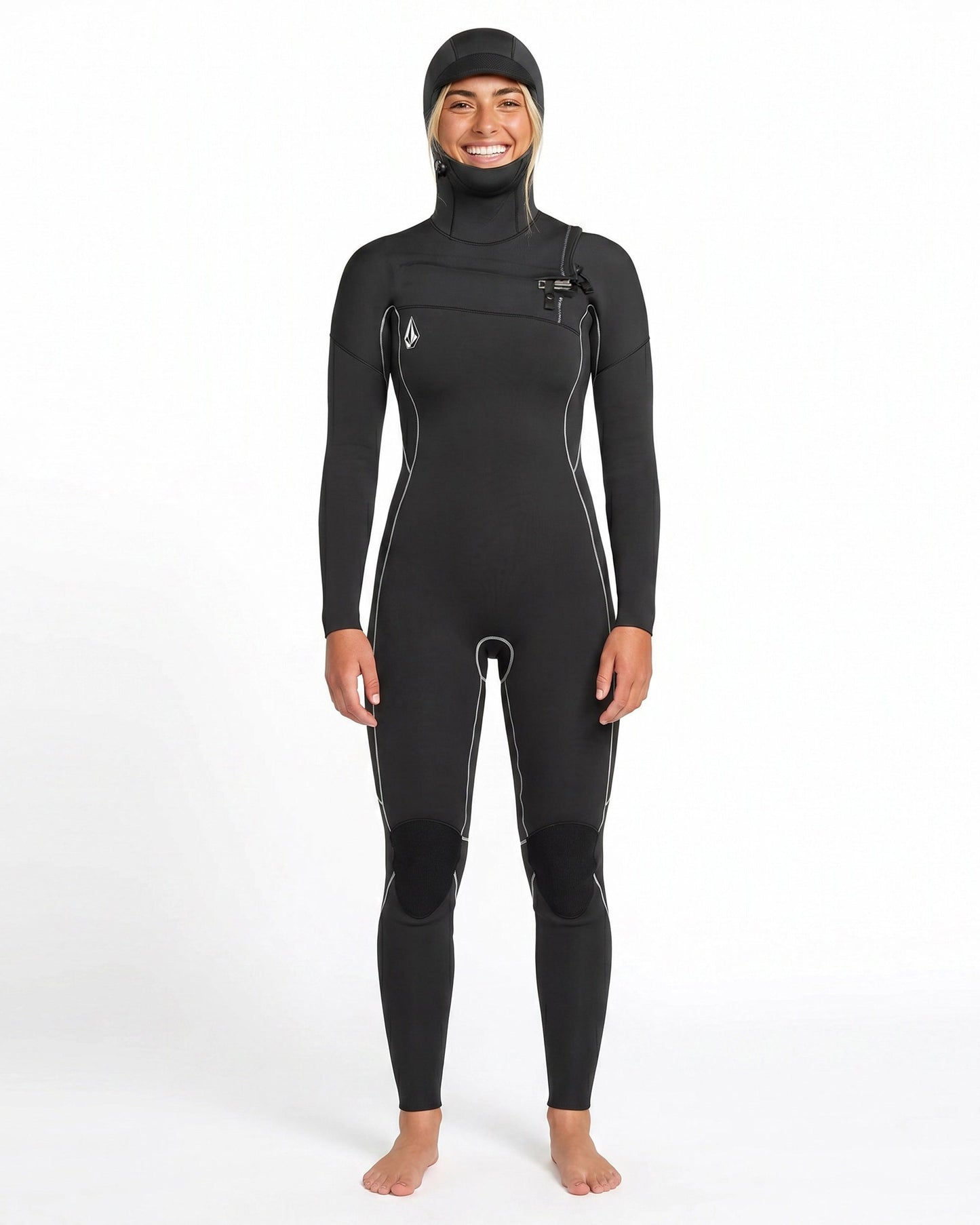 A person stands barefoot and smiling against a plain white background, wearing the Volcom Women's 4/3MM Modulator Chest Zip Hooded Full Wetsuit with white seams.