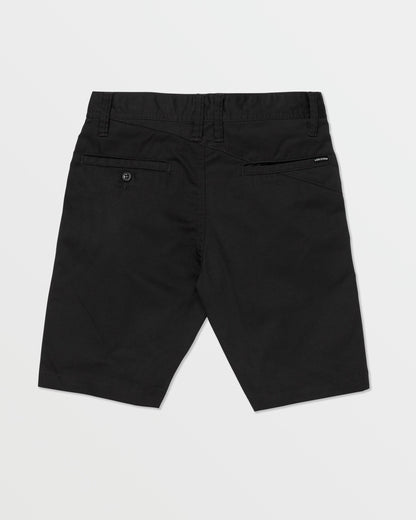 The Volcom Kids' Frickin Chino Shorts 16" are black, knee-length, shown from the back with a modern fit, belt loops, two rear pockets (one buttoned), and a black Volcom label above the right pocket. Shorts are laid flat on a white background.
