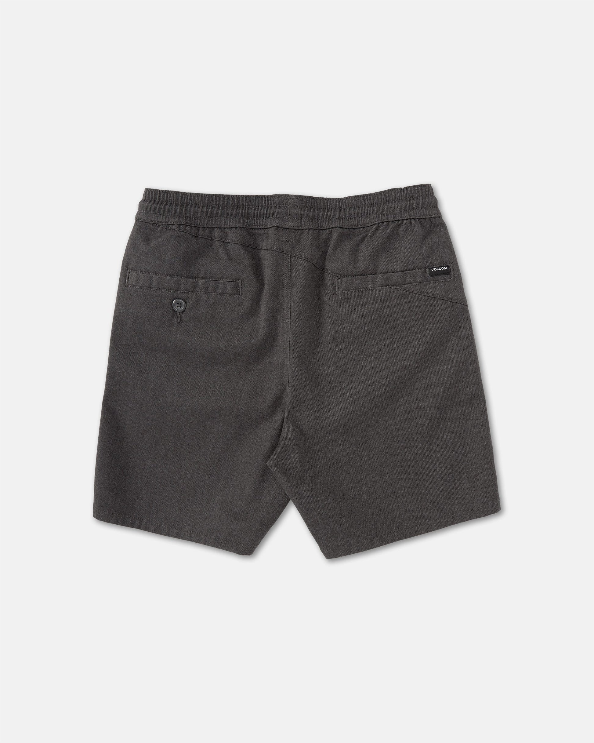 Back view of Volcom Kids' Big Boys' Frickin Elastic Waist Shorts in dark gray, featuring two back pockets (one with button) and a black brand tag above the right pocket. Made from recycled poly-cotton, shorts shown laid flat on a light surface.