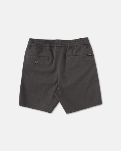 Back view of Volcom Kids' Big Boys' Frickin Elastic Waist Shorts in dark gray, featuring two back pockets (one with button) and a black brand tag above the right pocket. Made from recycled poly-cotton, shorts shown laid flat on a light surface.