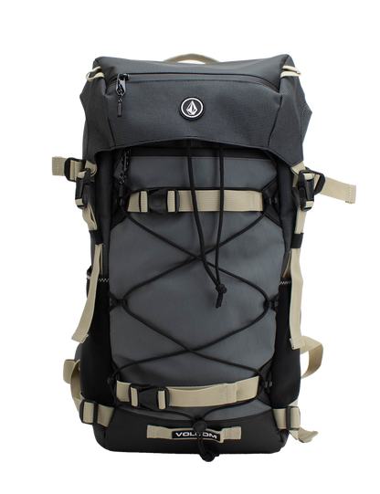 The Men's Peakstone Mountain Backpack by Volcom features a sleek black and gray design with beige straps, external bungee cords, and a convenient front zipper pocket. The iconic Volcom logo accents the top front flap, making this rugged daypack ideal for hiking excursions or resort riding adventures.