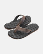 A pair of Volcom Men's Recliner black flip-flop sandals with brown straps and woven textured, extra-grippy soles is displayed on a plain light background.