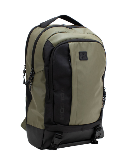 Introducing the Volcom Men's Venture Backpack in khaki and black, featuring a spacious 22L capacity with a front pocket, two side zippers, top handle, and a prominent black Volcom logo patch on the front. It includes a padded laptop sleeve for extra protection, a reinforced base for durability, and two bottom straps with buckles for added functionality.