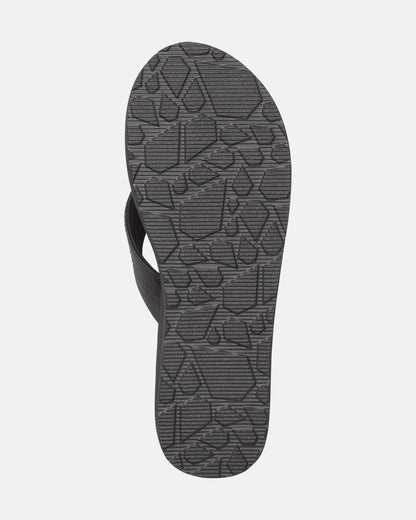 The image shows the bottom view of the Volcom Women's Boyfriends Thong sandal in black, featuring a geometric tread pattern on the sole and built-in arch support for comfort.
