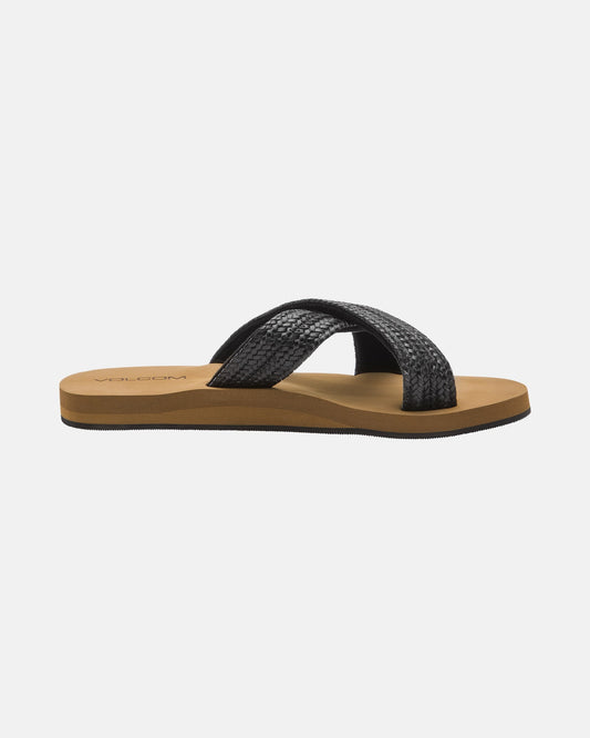 The Women's Volcom Double Cross Sandal by Volcom features a tan sole and two black textured crisscross straps, displayed from the side against a plain white background.