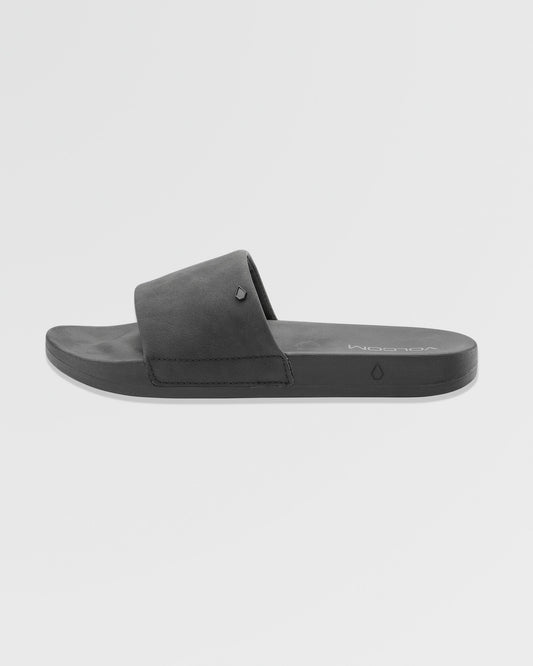The Women's Volcation Slides by Volcom are black slide sandals featuring a wide single strap and flat sole for everyday comfort, ideal for summer wear. Shown against a white background.