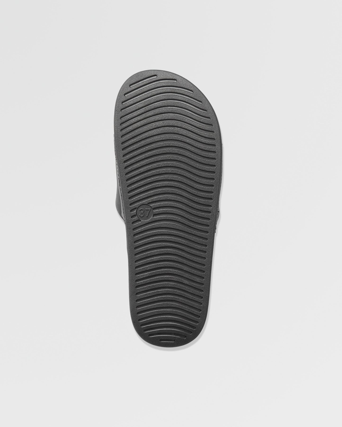 The image displays the black sole of Volcom Women's Volcation Slides, featuring horizontal grooves for traction and a size 37 mark. Set against a plain white background, it highlights everyday comfort and signature Volcom style.