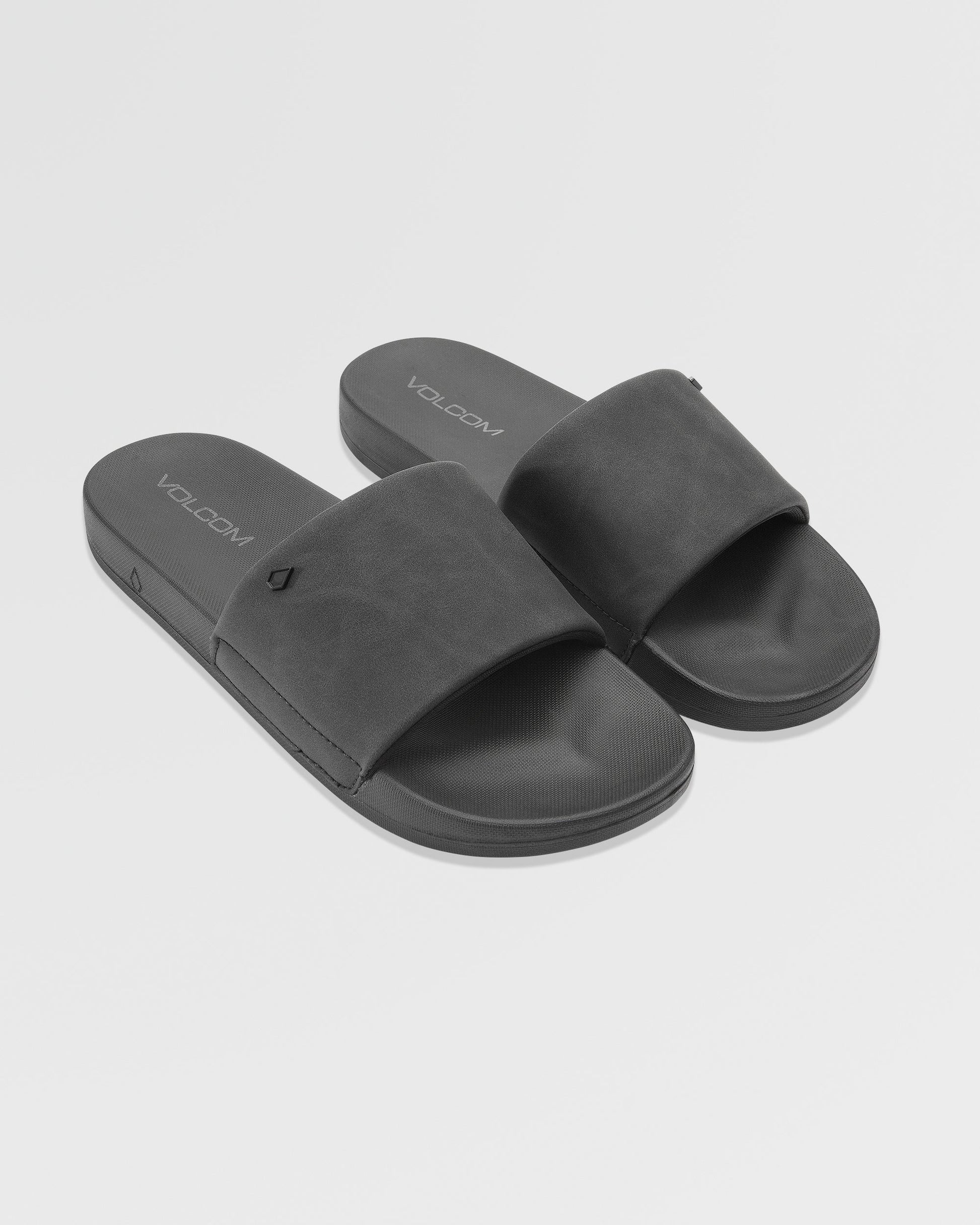 Women's Volcom Volcation Slides feature wide black straps and flat soles, angled on a plain white background. The insoles display the Volcom logo, highlighting signature style and comfort for everyday summer wear.