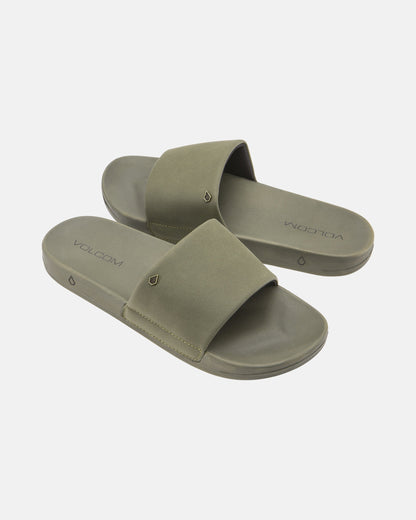 The Women's Volcom Volcation Slides feature olive green wide straps and flat soles, offering everyday comfort and classic Volcom style, shown against a white background.